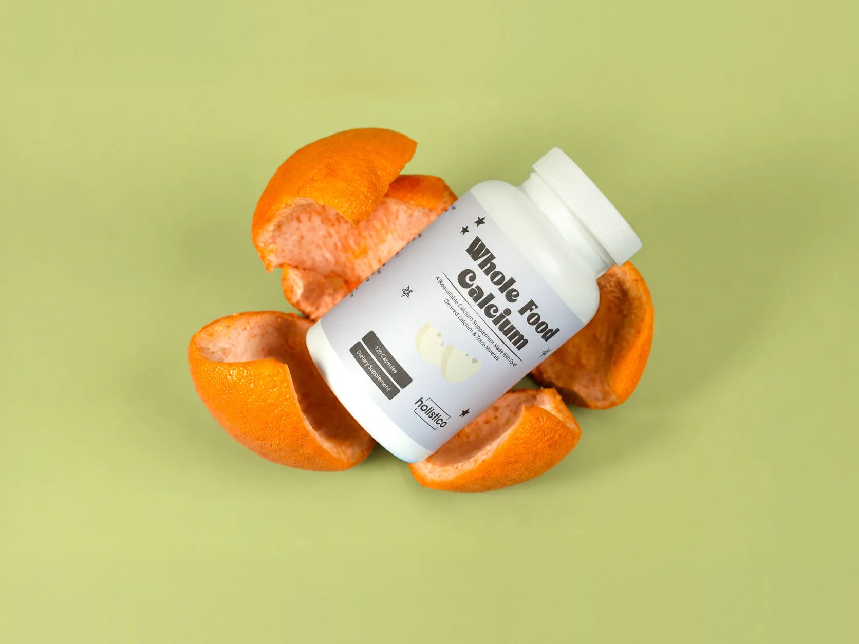 A bottle of Holistico Whole Food Calcium resting in pieces of orange peel on a green background
