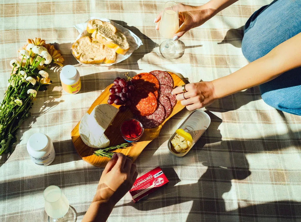 An overhead picnic spread on a tartan blanket with bottles of Holistico Whole Food Calcium and Whole Food Vitamin D beside a bunch of daisies