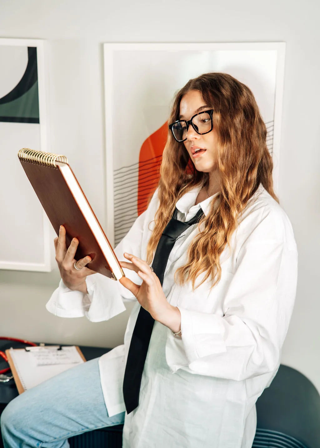A woman in a white shirt and tie reviewing a notebook, styled like a practitioner reading test results
