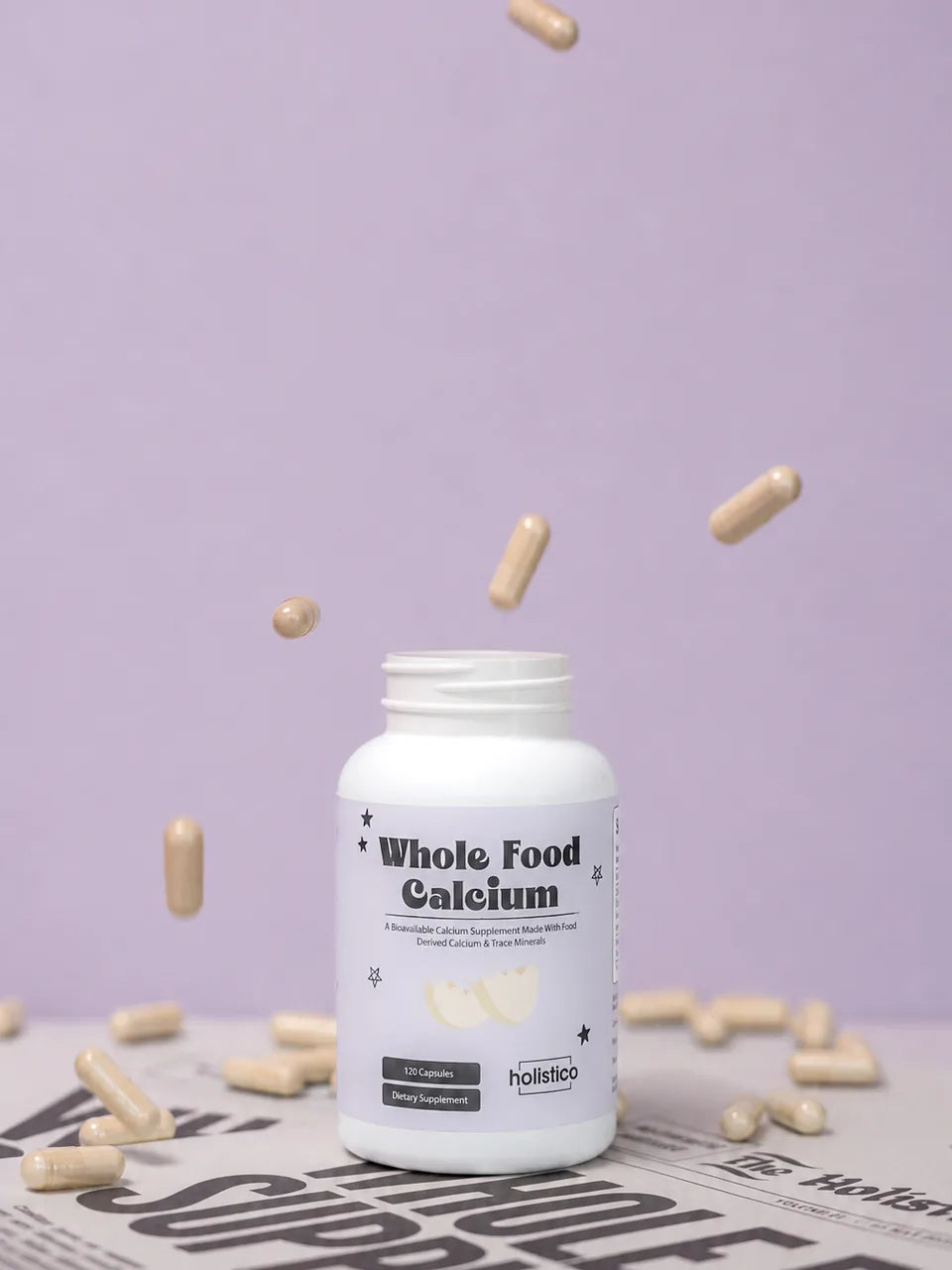 Capsules falling around a bottle of Whole Food Calcium on a newspaper, lilac background