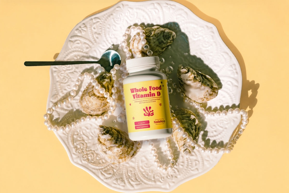 A bottle of Holistico Whole Food Vitamin D on an ornate white plate with oysters and pearls, on a yellow ground
