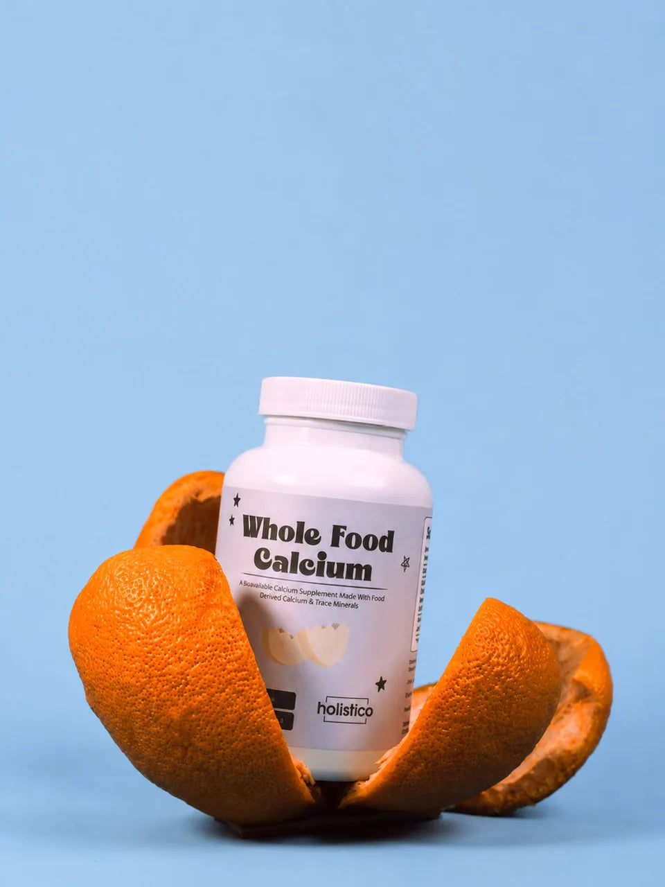 A bottle of Whole Food Calcium nestled inside an opened orange peel on a blue background
